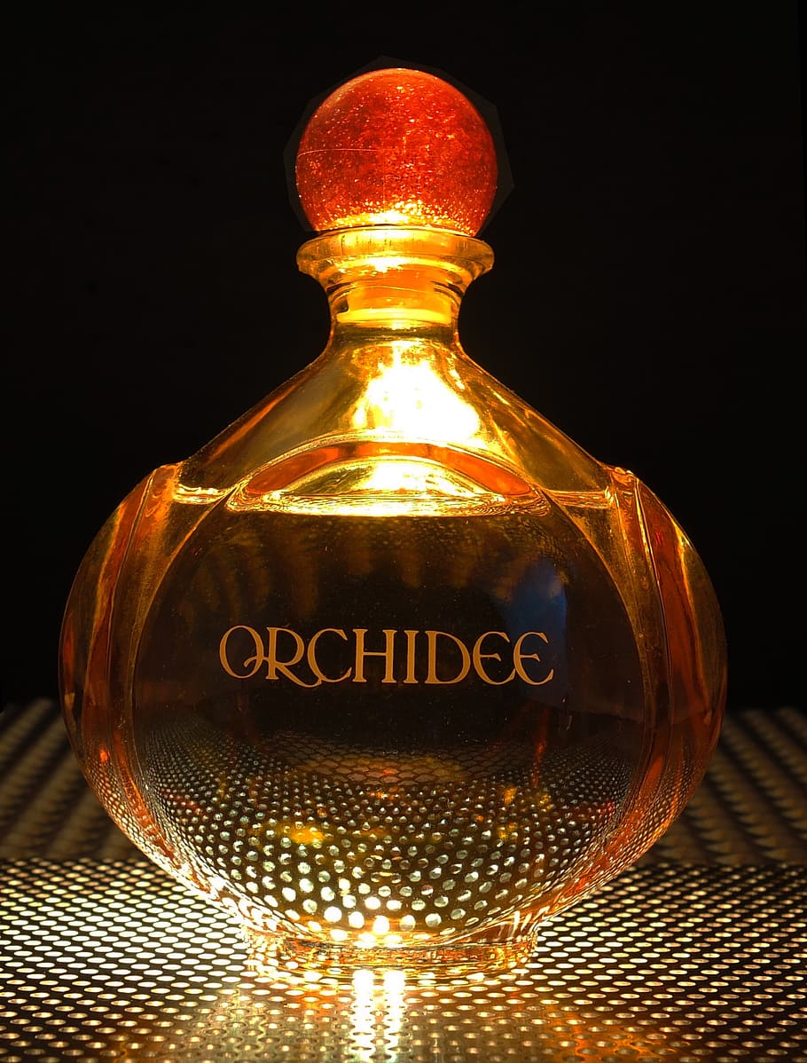 orange, orkidé glas duft flaske, parfume, flaske, lys nedenunder, indendørs, belyst, sort baggrund, meddelelse, vestlige script, ingen mennesker, tæt på, tekst, belysningsudstyr, studio skud, glas - materiale, glødende, nat, teknologi, metal, mønster, enkelt objekt, lys, lys pære, elektrisk lampe, 2K