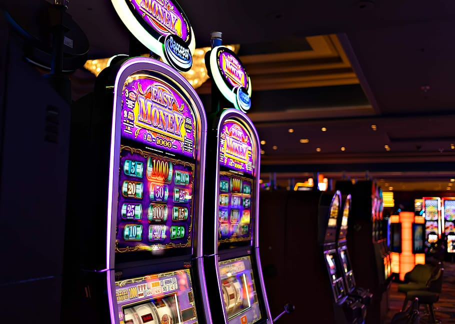 en arm bandit, flerfarvede, øst, penge spilleautomater, nat, mørk, maskine, lys, kasino, spilleautomat, gambling, belyst, multi farvet, held, indendørs, kunstkultur og underholdning, mulighed, ingen mennesker, fritidsaktivitet, fokus på forgrunden, fritidsspil, detail, tekst, tæt på, i en række, afspejling, lempelse, natteliv, 5K