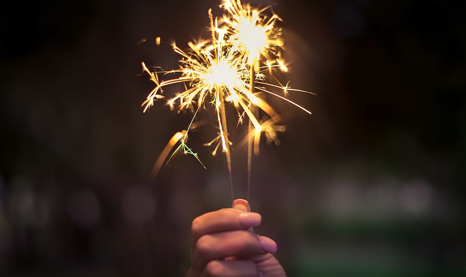 lys, hånd, mørk, sol, sløring, bokeh, lyse, brændt, fest, jul, sløret, aften, festival, fyrværkeri, flamme, blitz, blænding, guld, hed, belyst, uvæsentlige, luminescens, nytårsaften, udendørs, parti, stjernekastere, menneskelig hånd, bedrift, menneskelig kropsdel, stjernekaster, en person, bevægelse, brænding, begivenhed, glødende, fokus på forgrunden, nat, kunstkultur og underholdning, gnister, natur, fyrværkeri - menneskeskabt objekt, finger, 5K
