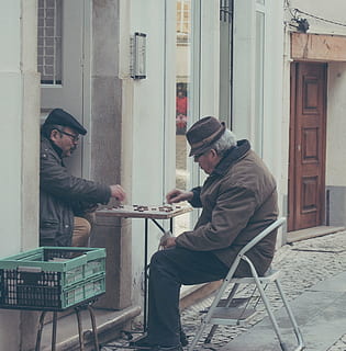 man, sitting, step stool, playing, chinese checkers, another, two, men, chair, front, table, board, game, house, door, window, people, chess, basket, outside, two people, only men, cap, side view, mid adult, adult, adults only, mature adult, real people, hat, young men, architecture, clothing, knit hat, built structure, lifestyles, seat, building exterior, casual clothing, full length, communication, warm clothing, 2K, CC0, public domain, royalty free