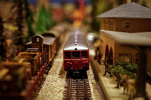 poc profund, focalitzar la fotografia, vermell, joguina de tren de plàstic, model de tren, model ferroviari, model, ferrocarril, tren, joguina, transport, rail, locomotora, pista, miniatura, pasatemps, estació, jugar, carruatge, petit, oci, infància, roda, elèctric, transport per ferrocarril, vies del ferrocarril, manera de transport, tren - vehicle, arquitectura, transport públic, enfocament selectiu, arbre, planta, viatjar, moviment, en moviment, a l'aire lliure, estructura construïda, naturalesa, cap gent, exterior de l'edifici, cotxe de ferrocarril, 4K, CC0, domini públic, lliure de regalies