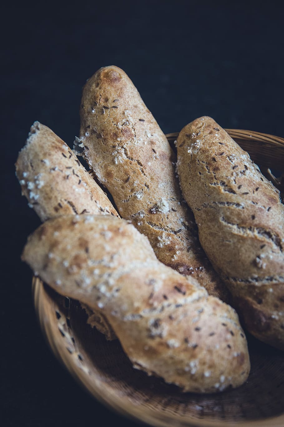 vier Sauerteigbrote, vier, gebacken, Gebäck, braun, Weidenkorb, Brot, Korb, Weizen, Dinkel, Laib, Lebensmittel, Essen und Trinken, Frische, drinnen, Nahansicht, Stillleben, schwarzer Hintergrund, Wohlbefinden, keine Leute, Studioaufnahme, gesundes Essen, fertig für den Verzehr, Tabelle, High Angle View, Fokus auf den Vordergrund, hausgemacht, selektiver Fokus, Versuchung, Snack, 5K