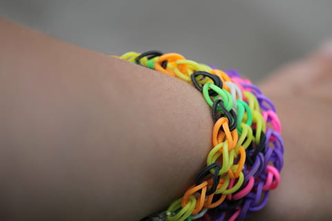 Webstuhl, Arm, Armband, Hand, Handgelenk, Schmuck, bunt, schwarz, Orange, Gelb, Grün, violett, Rosa, Farbe, Kind, schließen, Lebensfreude, basteln, mehrfarbig, menschliches Körperteil, Nahansicht, eine Person, drinnen, Erwachsene, Frau, Körperteil, Fokus auf den Vordergrund, menschliches Gelenk, menschliche Hand, Mode, Studioaufnahme, selektiver Fokus, Emotion, persönliches Accessoire, Blumenmuster, 4K, CC0, gemeinfrei, lizenzfrei