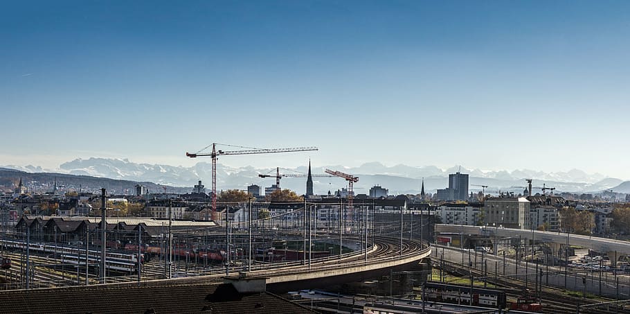 aèria, fotografia, buit, carretera, amb vistes, grues, blau, cel, durant el dia, arquitectura, edificis, infraestructura, torre, grua, construcció, pont, ciutat, urbà, muntanya, estructura construïda, transport, vista d’angle alt, manera de transport, transport per ferrocarril, naturalesa, exterior de l'edifici, viatjar, cap gent, dia, vies del ferrocarril, tren - vehicle, tren, edifici, pista, a l'aire lliure, paisatge urbà, 5K