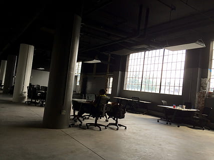 Mann, sitter, stol, vendt, bord, innsiden, bygning, person, rom, loft, kontor, studio, vindu, arbeid, lager, stort rom, søyle, kontorstol, kontorplass, Urban, fabrikk, arbeidsområde, tømme, innendørs, dag, arkitektur, full lengde, mennesker, sete, ekte folk, voksen, bygget struktur, menn, arkitektonisk kolonne, kvinner, sollys, virksomhet, gulv, arbeider, tak, 2K, CC0, offentlig domene, opphavsrett gratis