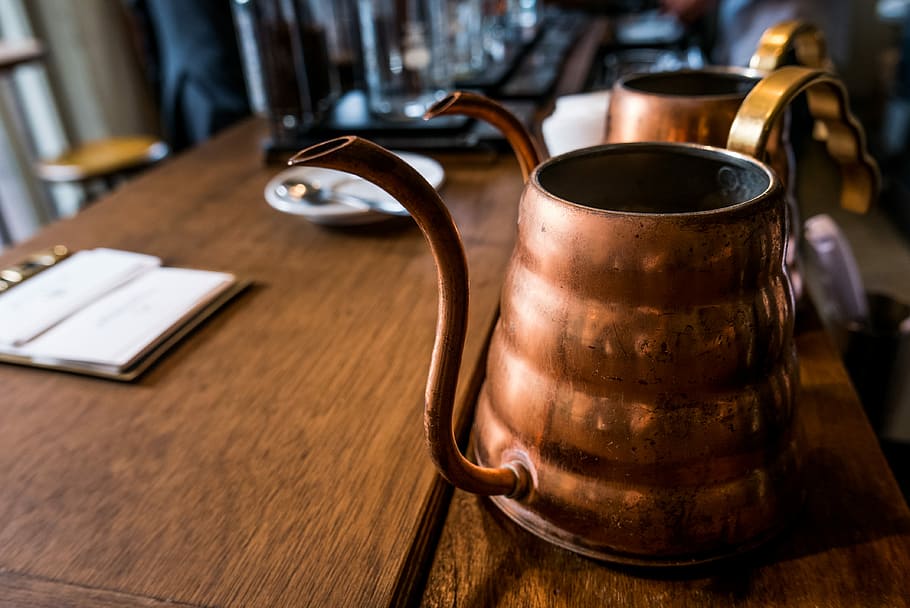 fotografia de canvi de inclinació, vintage, tetera de llautó, cafetera turca, te, coure, cafeteria, tetera, fusta, metall, gestionar, taula, bullidor d'aigua, llautó, llibre obert, olla, rústic, endins, material de fusta, menjar i beguda, a l'interior, beure, refresc, cap gent, centrar-se en primer pla, equipament per a la llar, marró, negocis, primer pla, dia, bar - establiment de begudes, estri de cuina, cuir, 4K