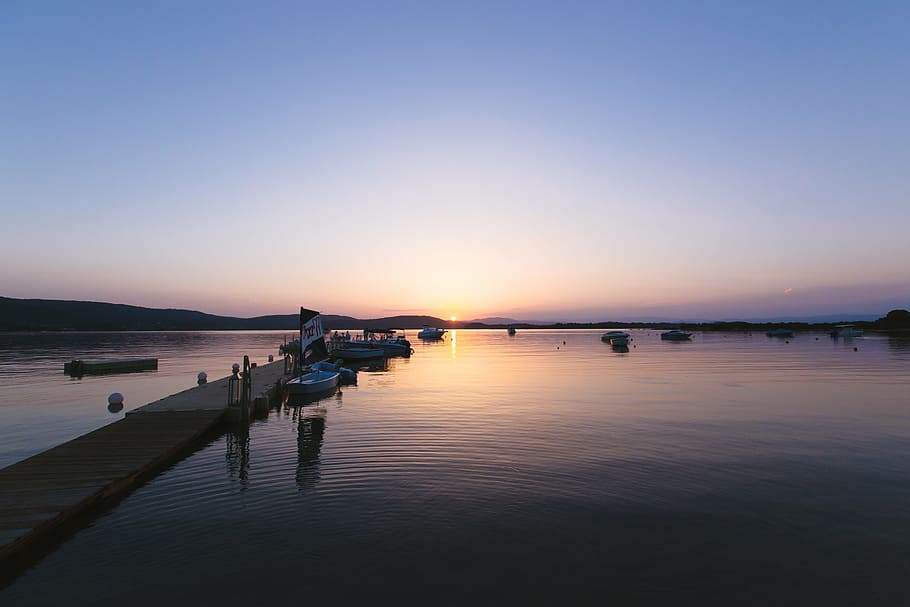 calm, body, water, brown, wooden, dock, boats, sunset, mountain, sky, sea, ocean, boat, flag, sailing, pathway, bridge, horizon, reflection, nautical vessel, outdoors, tranquility, nature, scenics, transportation, scenics - nature, tranquil scene, beauty in nature, mode of transportation, clear sky, travel, dusk, no people, blue, idyllic, 5K