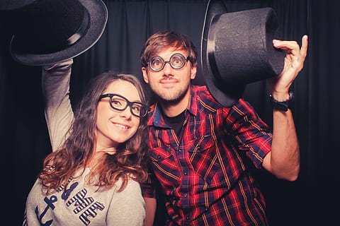 man, woman, holding, tap, hat, front, black, curtain, geek, magic, fun, nerd, colorful, play, faces, glasses, portrait, eyeglasses, looking at camera, men, smiling, young adult, young men, indoors, lifestyles, real people, adult, front view, happiness, two people, people, casual clothing, males, hipster - person, 2K, CC0, public domain, royalty free
