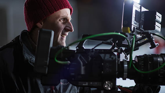 person, over, sort, grå, professionel, kamera, kamera mand, bag, video kamera, mand, professionel operatør, professionelt kamera, stadion kamera, film kameraman, kameramand, videography, kaukasiske, nat skyde, filmindustrien, kabel, rødt kamera, kantlys, tøj, en person, voksen, kunstkultur og underholdning, hovedskud, ydeevne, hat, indendørs, teknologi, fjernsynskamera, mikrofon, input enhed, ung voksen, portræt, beskæftigelse, studie, koncentration, bag scenen, filme, munden åben, sort baggrund, 4K, CC0, offentligt domæne, royaltyfrie
