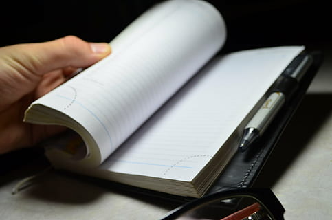 person, spejlvende, side, Bestil, notesbog, pen, hånd, dagbog, kontor, forretningsmand, arbejde, på arbejde, forhandlinger, briller, stil, årgang, åben bog, sort og hvid, undersøgelse, papir, menneskelig kropsdel, menneskelig hånd, indendørs, tæt på, skrivning, voksen, dokument, studio skud, mennesker, note pad, forretning, meddelelse, offentliggørelse, kuglepen, tekst, papirarbejde, sort baggrund, 2K, CC0, offentligt domæne, royaltyfrie