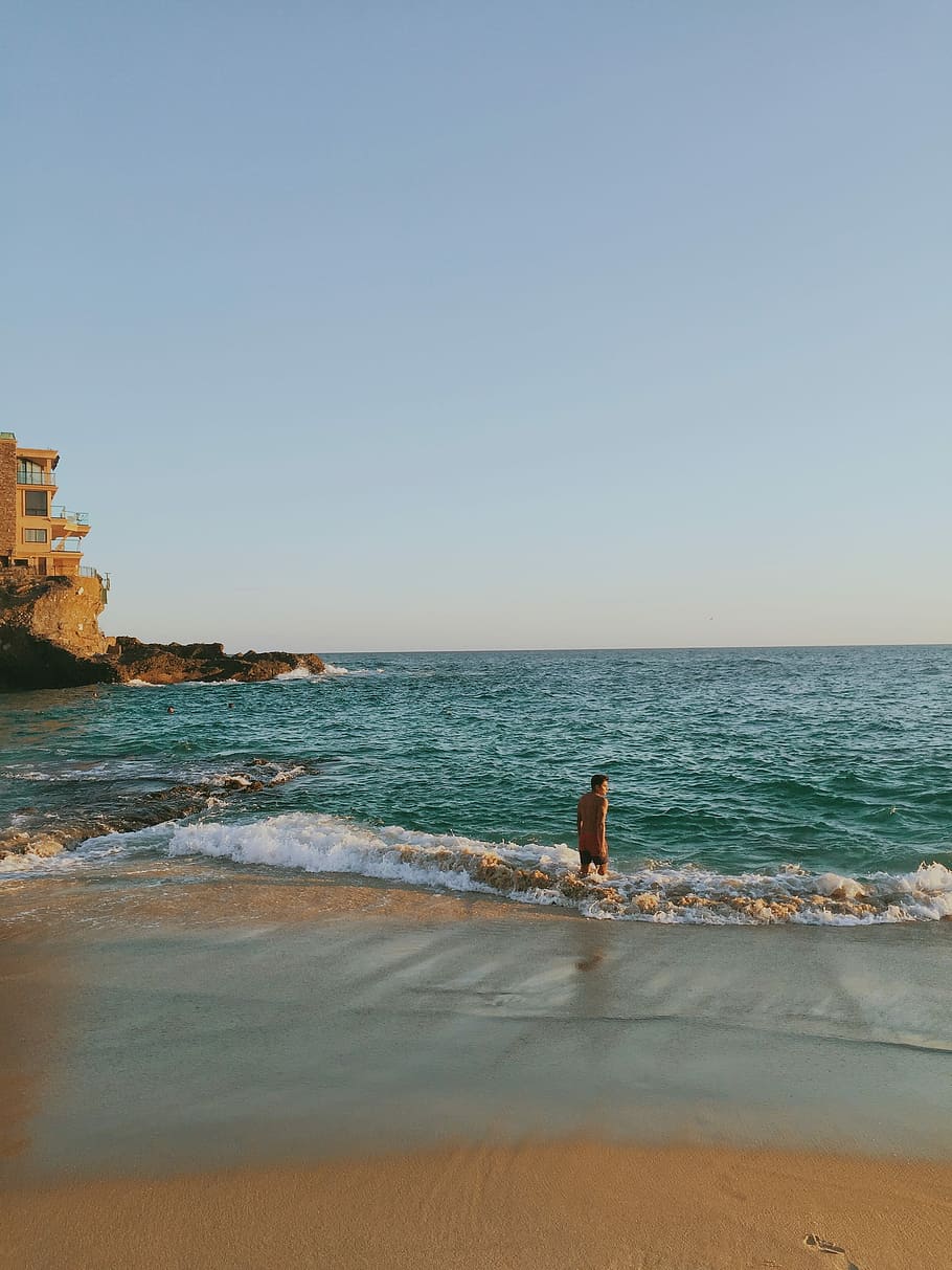 uomo, arancia, carro armato, superiore, nero, abito da scatti, in piedi, blu, mare, giorno, canotta, scatti, attrezzatura, mare blu, spiaggia, costa, acqua, onda, natura, cielo, roccia - oggetto, sabbia, all'aperto, Paesaggi, paesaggio, nessuno, cielo sereno, orizzonte sull'acqua, terra, scenics - natura, bellezza nella natura, orizzonte, copia spazio, persone reali, movimento, attività di svago, una persona, stili di vita, 2K
