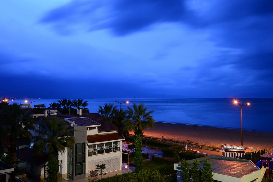 vista nocturna, platja, blau, mar, nit, posta de sol, vespre, exterior de l'edifici, arquitectura, estructura construïda, cel, aigua, il·luminat, clima tropical, núvol - cel, edifici, Palmera, arbre, ciutat, barri residencial, equips d’il·luminació, cap gent, casa, horitzó sobre l’aigua, a l'aire lliure, luxe, porpra, 5K