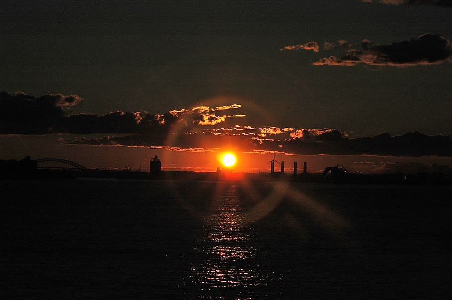 posta de sol, Sol ponent, halo, anell, brillar, configuració, sol, halo, anell, taronja, vespre, mar, reflexió, núvols, cel, nit, a l'aire lliure, transport, silueta, aigua, naturalesa, il·luminat, bellesa a la natura, cap gent, escenics - natura, arquitectura, estructura construïda, davant del mar, núvol - cel, exterior de l'edifici, color taronja, flare de la lent, 2K