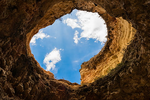 low, angle photo, cave, rock, formation, brown, hole, white, clouds, blue, sky, daytime, rock - object, cloud - sky, light at the end of the tunnel, rock formation, nature, day, sunlight, no people, solid, beauty in nature, shape, tranquility, land, scenics - nature, history, outdoors, the past, directly below, 5K, CC0, public domain, royalty free