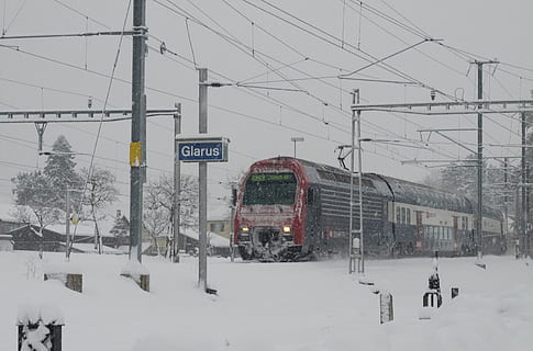 rosso, nero, treno, accanto, nevaio, SBB, s bahn, inverno, ferrovie federali svizzere, invernale, la neve, nevicata, Glarus, Svizzera, temperatura fredda, modo di trasporto, natura, mezzi di trasporto, architettura, elettricità, cavo, struttura costruita, cielo, esterno dell'edificio, copertura, Colore bianco, nevicando, linea elettrica, giorno, veicolo terrestre, bellezza nella natura, tempo estremo, nessuno, all'aperto, montagna innevata, Alimentazione elettrica, 2K, CC0, dominio pubblico, privo di copyright