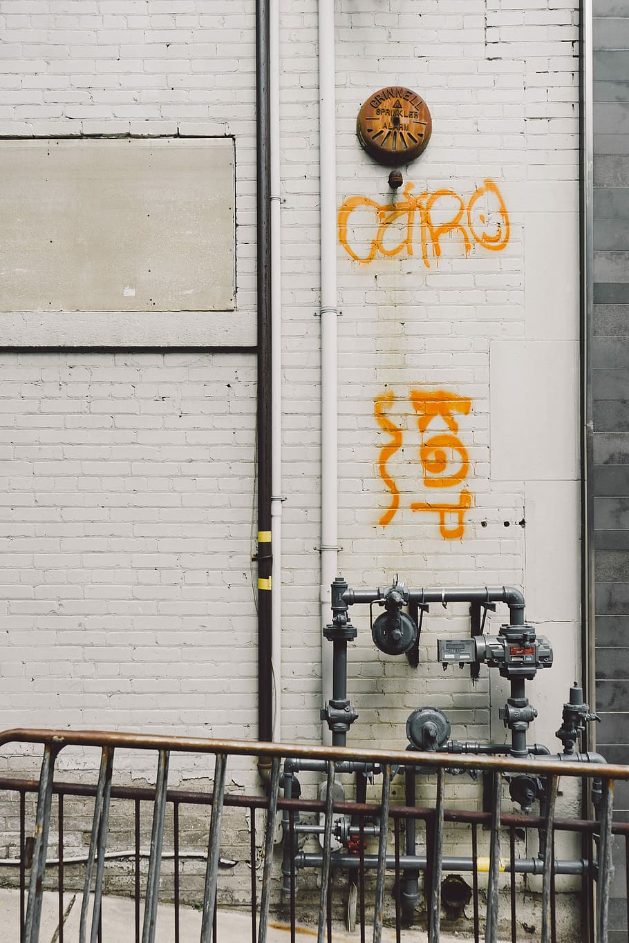 gris, canonada d’aigua d’acer, paret, canonada de metall, muntat, blanc, concret, graffiti, escriure, maons, canonada, barrera, tanca, barana, metre, alarma, timbre, porta, edifici, maó, cap gent, text, metall, dia, comunicació, funció de construcció de parets, arquitectura, estructura construïda, tub de tub, exterior de l'edifici, a l'aire lliure, seguretat, protecció, guió occidental, entrada, indústria, tancat, Color blanc, 5K