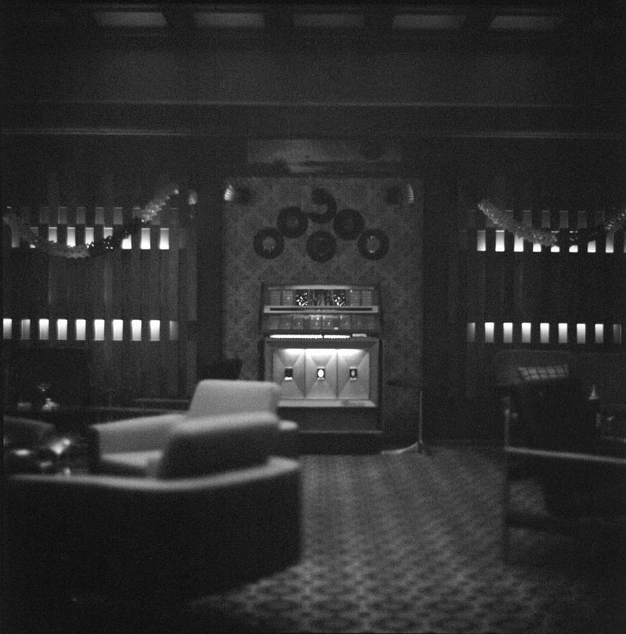 fotografia en escala de grisos, cadires, llar de foc, habitació, juke box, música, vell, vintage, blanc i negre, il·luminat, a l'interior, cultura i entreteniment artístic, tecnologia, cap gent, televisor, arquitectura, estructura construïda, nit, equips d’il·luminació, pantalla, habitació domèstica, en fila, cinema, control, mobles, seient, pantalla del dispositiu, vida nocturna, 5K