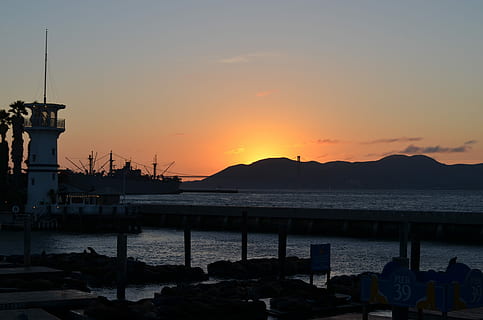 Sonnenuntergang, Leuchtturm, Dämmerung, Abend, Abendsonne, golden, abendstimmung, Meer, Wasser, Blau, Seebrücke, orange Farbe, Silhouette, Wasserfahrzeug, Hafen, Himmel, Schönheit in der Natur, Natur, Transport, Szenen - Natur, ruhige Szene, Berg, Land, Ruhe, Transportmittel, Strand, die Architektur, festgemacht, keine Leute, draußen, 2K, CC0, gemeinfrei, lizenzfrei