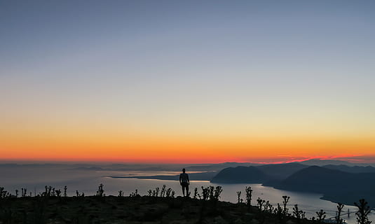 silhuet foto, mand, stående, bjerg, silhuet, klint, leder, kystlinier landskabsfotografering, Foto, person, grå, oransje himmel, tusmørke, solnedgang, natur, landskab, skumring, udendørs, himmel, scenics, solopgang - daggry, orange farve, baggrundsbelyst, skønhed i naturen, scenics - natur, fritidsaktivitet, rolig scene, livsstil, ro, rigtige mennesker, mennesker, ikke-urbane scene, kopiere plads, idyllisk, herrer, uigenkendelig person, 4K, CC0, offentligt domæne, royaltyfrie