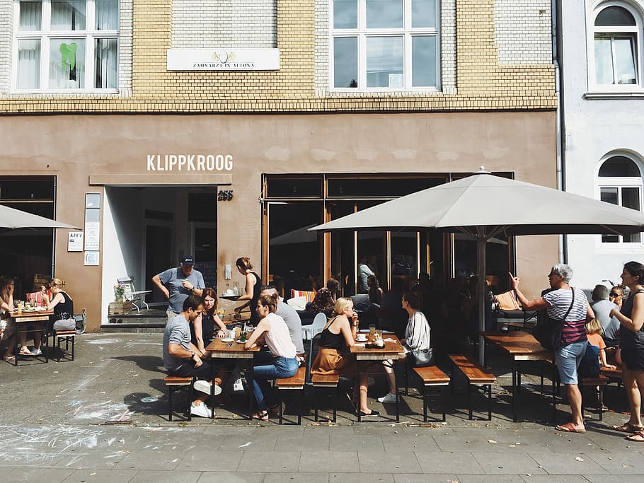 grup, gent, assegut, bancs, taules, al costat, front de la botiga klippkroog, durant el dia, seure, pati, conjunt, cafeteria, persona, paraigua, taula, restaurant, edifici, a l'aire lliure, cafè, beure, fora, banc, jardí de cervesa, exterior, vorera, arquitectura, estructura construïda, exterior de l'edifici, grup de persones, persones reals, seient, homes, ciutat, adult, multitud, dones, gran grup de persones, estils de vida, cadira, 4K