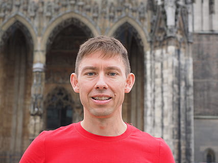 Mann, rot, Hemd mit Rundhalsausschnitt, lächelnd, neben, grau, Beton, Gebäude, Mensch, zufrieden, gesegnet, Person, Gesicht, Porträt, Augen, Mund, Nase, Ohren, Lächeln, frontal, Kopfschuss, eine Person, Kamera betrachten, die Architektur, Erwachsene, Lebensstile, Vorderansicht, gebaute Struktur, Reiseziele, echte Menschen, Tag, junger Erwachsener, Gebäudehülle, Tourismus, Männer, Bogen, 4K, CC0, gemeinfrei, lizenzfrei