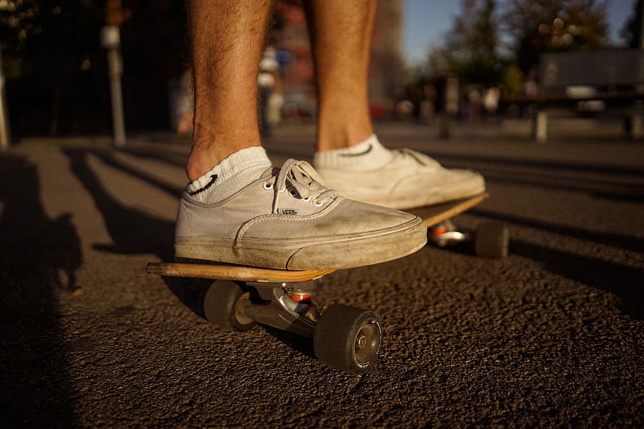 person, iført, hvid, ridning, skateboard, varevogne, autentisk, udendørs, menneskelige ben, udøver, sport, sund livsstil, sportssko, mennesker, en person, livsstil, menneskelige fod, hunner, løbe, skateboarding, urban scene, handling, herrer, Kvinder, sko, ung voksen, uigenkendelig person, sports træning, lavt afsnit, menneskelig kropsdel, kun en mand, kropsdel, transportmidler, fritidsaktivitet, bevægelse, rigtige mennesker, dag, by, sollys, vej, gade, afslappet tøj, transportform, hjul, jeans, menneskelig lem, 5K