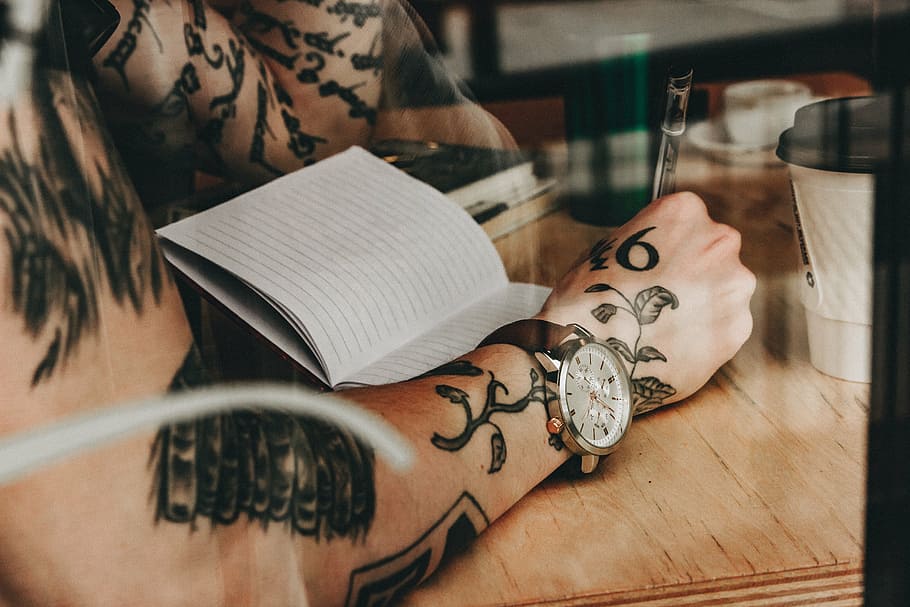 persona, escriure, governat, paper, gent, home, lectura, llibre, fusta, taula, canell, veure, cos, tatuatge, art, part del cos humà, a l'interior, creativitat, art i artesania, una persona, mà humana, mà, primer pla, estils de vida, part del cos, centrar-se en primer pla, persones reals, adult, moda, text, disseny, activitat d'oci, comunicació, motiu floral, 5K