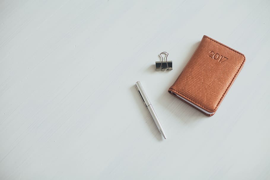gris, ploma de torsió, al costat, marró, cartera de cuir, clip de paper, blanc, superfície, quadern, notes, diari, bolígraf, calendari, curs, aglutinant, taula, escriure, a l'interior, còpia espai, natura morta, vista d’angle alt, cap gent, color taronja, fons blanc, equipament, metall, tir de l'estudi, art i artesania, eina, color plata, interior de casa, publicació, diy, dos objectes, dia, eina de treball, millores per a la llar, 5K