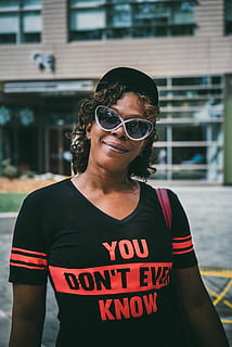 person, wearing, black, crew-neck shirt, orange, ever, know, text, crew-neck, shirt, people, outdoors, women, sunglasses, one Person, females, smiling, young Adult, waist up, mid adult, portrait, glasses, real people, front view, fashion, leisure activity, casual clothing, lifestyles, architecture, building exterior, standing, focus on foreground, built structure, day, hairstyle, 4K, CC0, public domain, royalty free