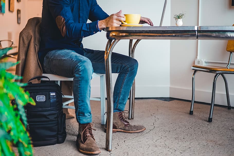 person, sidder, bedrift, gul, te kop, mand, iført, blå, kjole skjorte, denim, monteret, jeans outfit, hvid, stol, sidder ved bordet, bord, kop, kaffe, ben, en person, voksen, afslappet tøj, sæde, lavt afsnit, krus, fuld længde, sko, drikke, kaffekop, kaffe - drikke, livsstil, fritidsaktivitet, mad og drikke, jeans, 4K