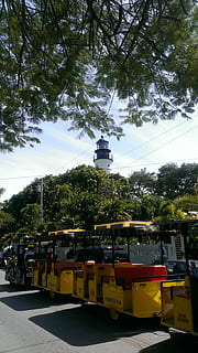 key, west, lighthouse, conch, train, island, ocean, outside, tree, mode of transportation, plant, transportation, day, nature, sky, outdoors, public transportation, no people, yellow, sunlight, land vehicle, in a row, architecture, nautical vessel, growth, city, road, 2K, CC0, public domain, royalty free