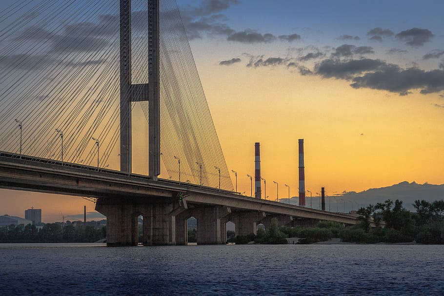bridge over water, hanging, bridge, dawn, river, sunset, factory, chimneys, water, architecture, sky, built structure, transportation, connection, nature, bridge - man made structure, building exterior, cloud - sky, no people, city, outdoors, travel destinations, orange color, waterfront, architectural column, 5K