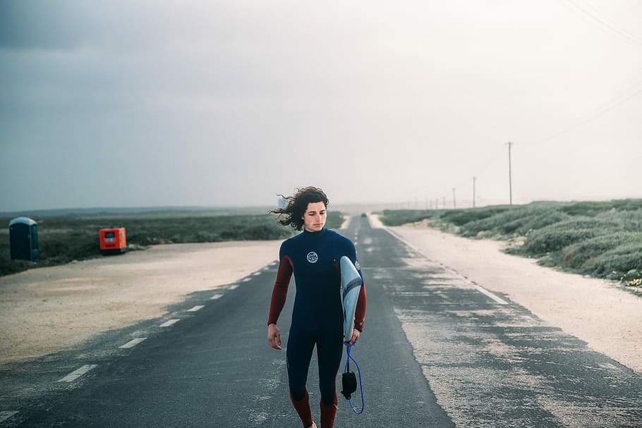 person, gå, vej, transporterer, surfbræt, stående, asfaltvej, surf, mand, vind, portræt, en person, ung voksen, transportmidler, himmel, fuld længde, natur, forfra, afslappet tøj, dag, livsstil, kigger på kameraet, voksen, by, fritidsaktivitet, på farten, unge mænd, udendørs, faldende perspektiv, 5K