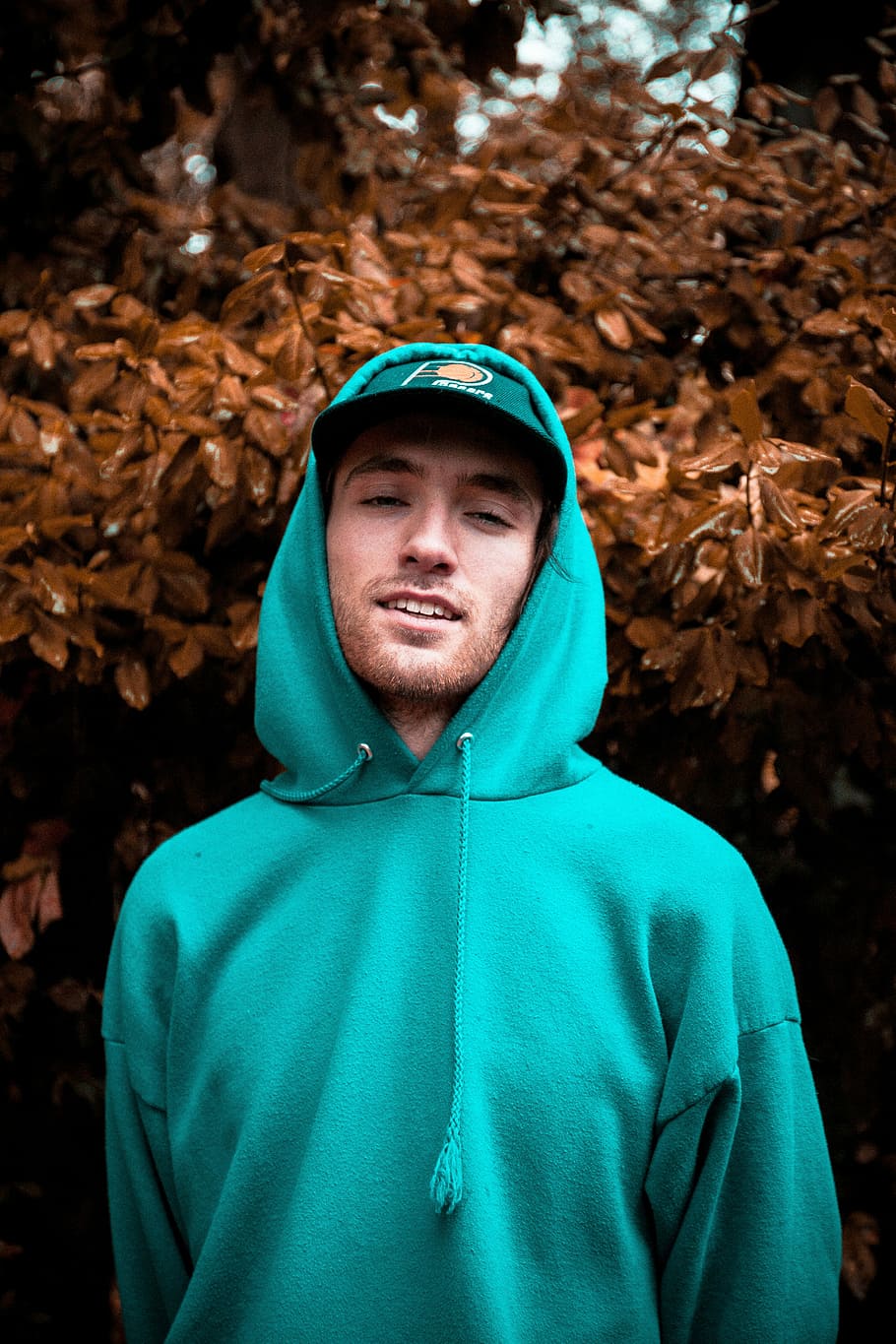 selektiv, fokus fotografering, smilende, mand, iført, trøje pullover hoodie, pacers, monteret, kasket, bag, Brun, blade, portræt, hat, træ, natur, hættetrøje, blå, skæg, humør, han-, krikand, efterår, blad, dreng, en person, forfra, kigger på kameraet, rigtige mennesker, ung voksen, unge mænd, fokus på forgrunden, taljen op, plante del, fritidsaktivitet, stående, dag, grøn farve, livsstil, tøj, udendørs, hætte - tøj, varme tøj, lave om, 5K
