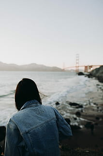 person, sitting, sea, overlooking, red, bridge, daytime, woman, wearing, blue, denim jacket, rock, seashore, river, water, cloud, landscape, rear view, sky, lifestyles, real people, leisure activity, one person, nature, clear sky, land, clothing, day, copy space, women, focus on foreground, outdoors, beauty in nature, looking at view, hood - clothing, warm clothing, 4K, CC0, public domain, royalty free