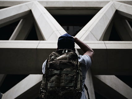 architecture, backpack, building, man, person, rear view, built structure, one person, building exterior, day, real people, men, standing, outdoors, occupation, lifestyles, clothing, sunlight, railing, nature, focus on foreground, bridge, uniform, 4K, CC0, public domain, royalty free