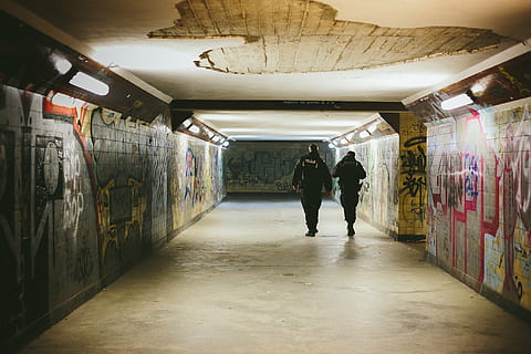 concrete surface, graffiti, night, patrol, people, police, police officers, train station, tunnel, underground, walking, indoors, rear view, architecture, full length, subway, the way forward, real people, direction, illuminated, men, built structure, lifestyles, wall - building feature, women, public transportation, ceiling, underpass, underground walkway, 2K