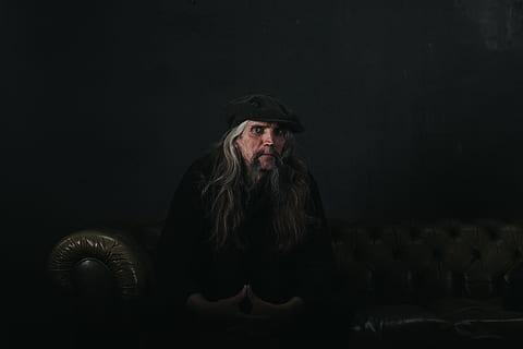om, ședință, maro, canapea, gri, om în negru, costum negru, fotografie, caucazian, pălărie, oameni, o persoana, etnie caucaziană, masculi, bărbați, doar adulți, par lung, adult, doar un singur om, portret, îmbrăcăminte, vedere din față, privind camera, Păr facial, barbă, în interior, Fundal negru, arta culturii și divertismentului, matur adult, capac, Piele, coafura, contemplare, 5K, CC0, domeniu public, fără drepturi de autor