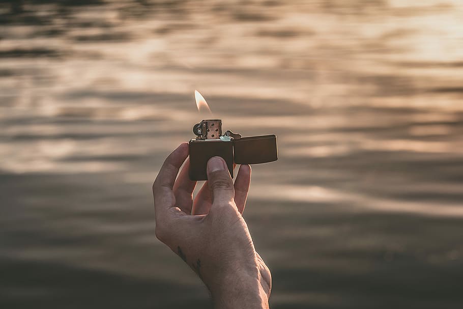 person, bedrift, tændte, sort, flip, lighter, ild, flamme, hånd, hånd tatovering, vand, afspejling, sø, lys, menneskelig hånd, menneskelig kropsdel, natur, brænding, en person, hav, fokus på forgrunden, jord, brand - naturligt fænomen, solnedgang, himmel, strand, voksen, meddelelse, menneskelig lem, aggression, arme hævet, 5K