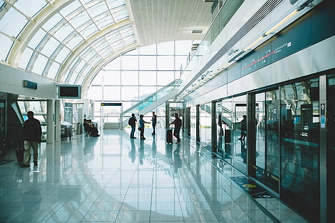 person, standing, holding, luggage, hallway, six, people, airport, travel, transportation, trip, windows, suitcase, blurred motion, passenger, indoors, journey, business travel, leaving, commuter, walking, architecture, group of people, built structure, modern, men, crowd, real people, glass - material, flooring, mode of transportation, day, large group of people, adult, airport departure area, ceiling, station, airport terminal, arrival, 2K
