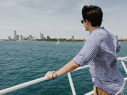 boat, buildings, man, ocean, person, sea, water, nautical Vessel, travel, people, outdoors, built structure, architecture, building exterior, city, sky, real people, nature, one person, lifestyles, leisure activity, transportation, day, young adult, building, standing, skyscraper, office building exterior, cityscape, 2K