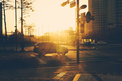 silver suv, crossing, pedestrian, lane, golden, hour, gray, suv, towards, street, road, intersection, sunset, city, urban, traffic lights, architecture, outdoors, city life, building exterior, built structure, transportation, sunlight, nature, sky, footpath, mode of transportation, tree, lens flare, one person, crosswalk, car, city street, sun, light, 5K