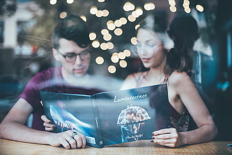 Mann, sitter, ved siden av, kvinne, lesning, kvinne leser luminescens bok, bokeh lys, bakgrunn, portrett, par, refleksjon, briller, to mennesker, ung voksen, voksen, menn, unge kvinner, kvinner, samvær, belyst, liming, fokusere på forgrunnen, holding, teknologi, innendørs, belysningsutstyr, mennesker, ekte folk, smilende, følelse, hunner, glass, parforhold, 5K, CC0, offentlig domene, opphavsrett gratis