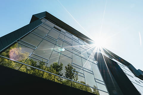 fotografia d'angle baix, de gran alçada, comercial, edifici, durant el dia, baix, foto d'angle, gris, concret, cel blau, reflexió, finestra, arquitectura, arquitectònic, exterior, façana, resplendor, modern, estructura, vidre, cel, sol, arbre, futurista, estructura construïda, exterior de l'edifici, ciutat, exterior d’edifici d’oficines, vista d’angle baix, oficina, naturalesa, llum solar, negocis, flare de la lent, vidre - material, blau, barri residencial, dia, gratacels, cap gent, a l'aire lliure, brillant, paisatge urbà, districte financer, acer, 5K, CC0, domini públic, lliure de regalies