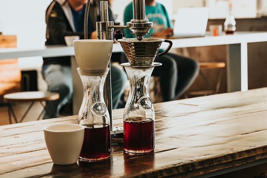 zwei, klar, Glasflaschen, rot, Flüssigkeiten, braun, hölzern, Zähler, Hurrikan-Brille, Kaffee, Cafe, kalte Presse, tropfen, Filter, Getränk, Erfrischung, Essen und Trinken, Tabelle, Kaffee trinken, Fokus auf den Vordergrund, Frische, Geschäft, drinnen, Becher, Tasse, Stillleben, Kaffeetasse, Nahansicht, zufällige Menschen, Café, Restaurant, Glas, Barista, Bartheke, Tablett, 5K