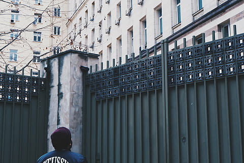 person, standing, beside, steel gate, man, blue, shirt, front, green, metal, gate, fence, entrance, buildings, architecture, city, day, outdoors, one person, real people, people, adult, adults only, built structure, building exterior, window, building, lifestyles, leisure activity, men, residential district, rear view, low angle view, women, headshot, warm clothing, 4K, CC0, public domain, royalty free