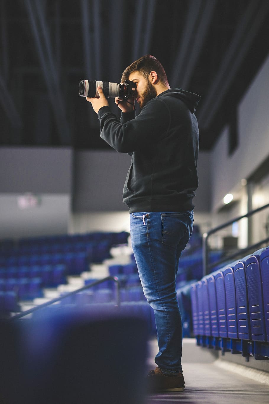 home, presa, foto, estadi, utilitzant, càmera dslr, teleobjectiu, persona, càmera, seients, fila, equipament, fent una foto, moda, estil, tecnologia, model, pose, equip de vídeo, càmera de vídeo, equip de videografia, videògraf, videografia, vídeo, adult jove, una persona, de peu, a l'interior, roba casual, home jove, homes, activitat d'oci, adult, esport, cultura i entreteniment artístic, longitud completa, persones reals, habilitat, nit, il·luminat, música, texans, etapa, 5K