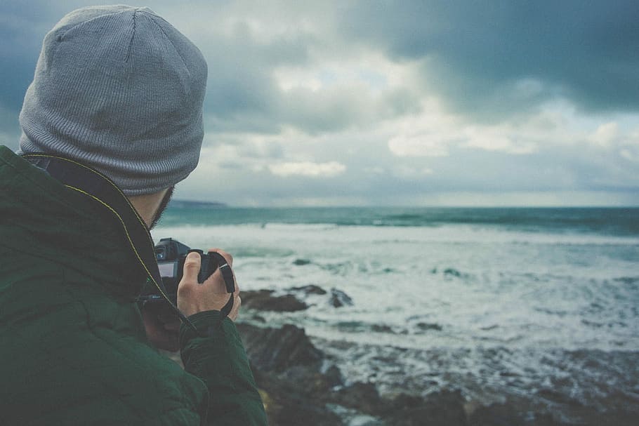 Mann, halten, DSLR-Kamera, nehmen, Bild, Strandwellen, Foto, Ozeanwelle, grau, Wolken, Wolke, Strand, Kamera, Ozean, Rock, Fotograf, Meer, Horizont, männlich, Person, Hut, Gurt, halt, Himmel, Wasser, Land, Aktivität, Technologie, wolke - himmel, eine Person, Kleidung, Natur, Fotografie-Themen, Erwachsene, Kapuze, Männer, Freizeitbeschäftigung, kabellose Technologie, Kapuze - Kleidung, Horizont über Wasser, draußen, 1080P