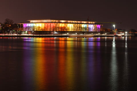 Kennedy Center, encès, edifici de vidre, nit, fosc, llums, reflexió, llac, il·luminat, aigua, arquitectura, exterior de l'edifici, estructura construïda, ciutat, cap gent, davant del mar, naturalesa, destinacions de viatge, cel, riu, transport, multicolor, porpra, edifici, equips d’il·luminació, vida nocturna, 5K, CC0, domini públic, lliure de regalies