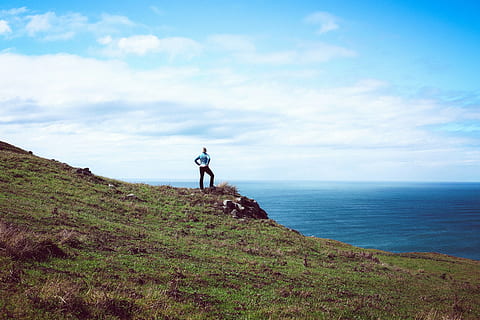 person, standing, grass, edge, mountain, highland, green, outdoor, adventure, rocks, sea, ocean, water, coast, blue, sky, clouds, landscape, nature, people, woman, horizon over water, scenics, real people, one person, leisure activity, beauty in nature, lifestyles, scenics - nature, land, full length, cloud - sky, day, tranquility, tranquil scene, non-urban scene, horizon, outdoors, 5K, CC0, public domain, royalty free